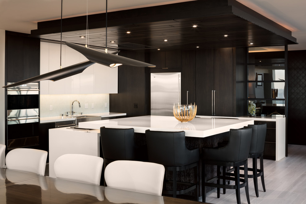 This is an example of a large contemporary l-shaped eat-in kitchen in Milwaukee with a farmhouse sink, flat-panel cabinets, dark wood cabinets, quartz benchtops, white splashback, glass tile splashback, stainless steel appliances, light hardwood floors and multiple islands.