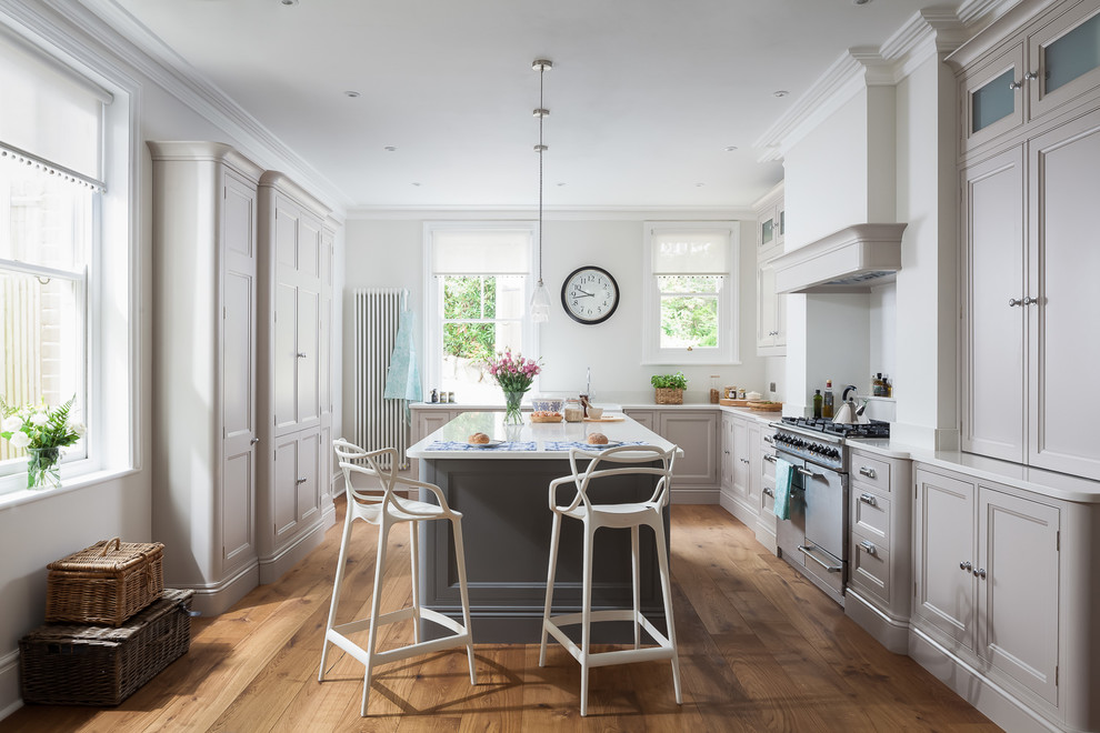 Mid-sized traditional l-shaped kitchen in Sussex with a farmhouse sink, recessed-panel cabinets, grey cabinets, stainless steel appliances, light hardwood floors, with island and brown floor.