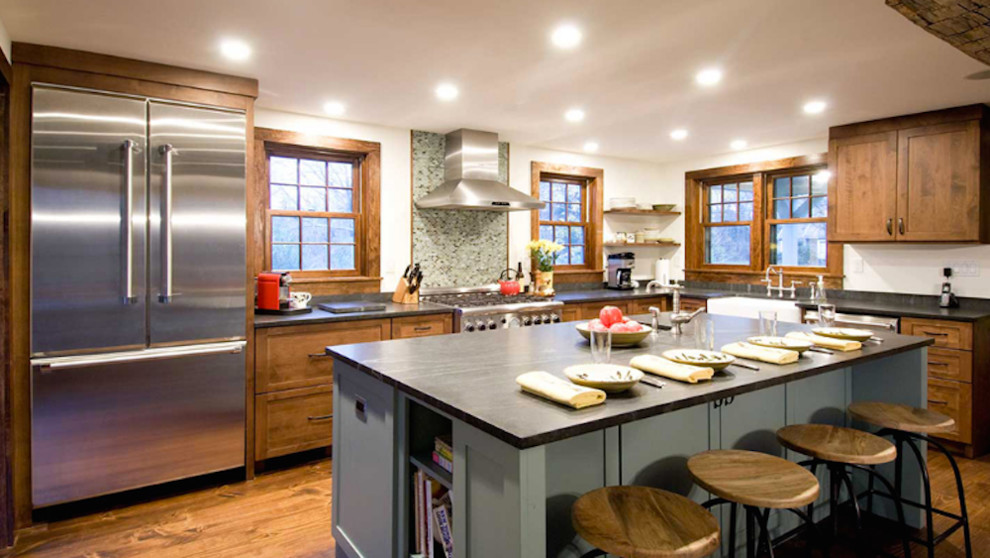This is an example of a country l-shaped open plan kitchen in New York with shaker cabinets, medium wood cabinets, multi-coloured splashback, stainless steel appliances, medium hardwood floors, with island and an undermount sink.