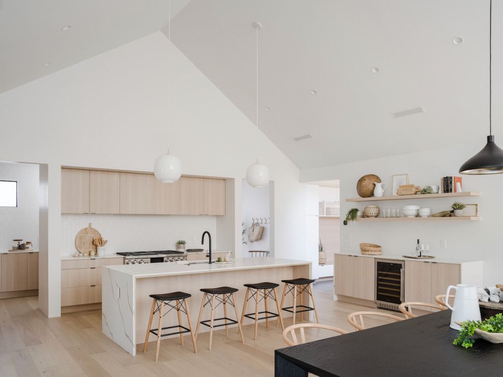 This is an example of a scandinavian open plan kitchen in Phoenix with a single-bowl sink, flat-panel cabinets, light wood cabinets, quartz benchtops, white splashback, porcelain splashback, panelled appliances, light hardwood floors, with island, white benchtop and vaulted.