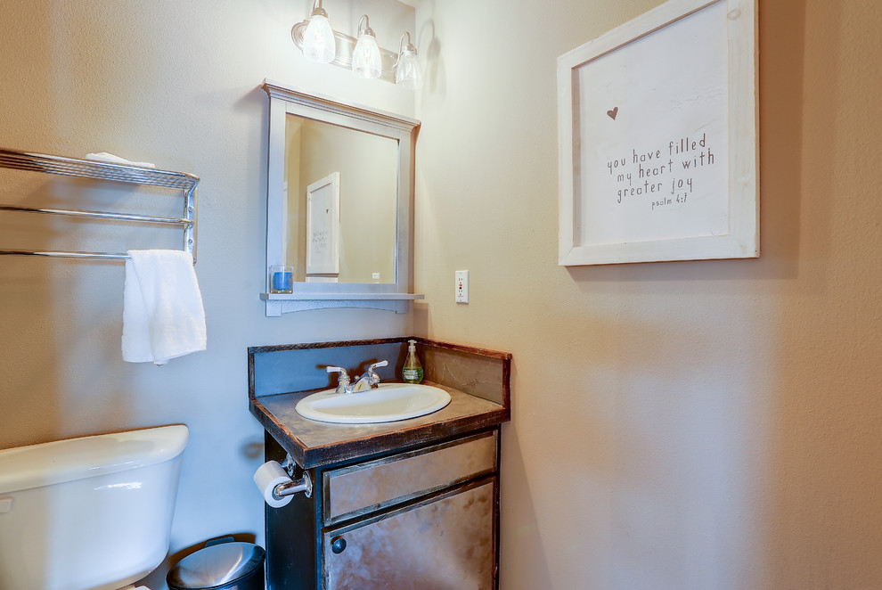 This is an example of a small country bathroom in Other with distressed cabinets, flat-panel cabinets, a one-piece toilet, a drop-in sink, stainless steel benchtops, grey benchtops and beige walls.
