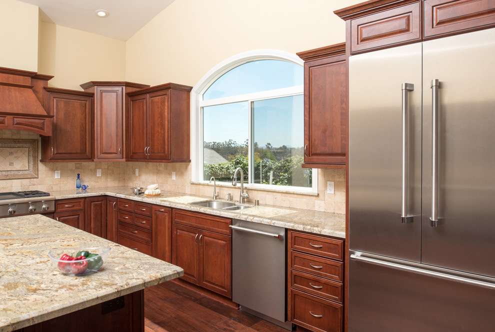 Inspiration for an expansive traditional l-shaped open plan kitchen in San Diego with raised-panel cabinets, dark wood cabinets, granite benchtops, beige splashback, stone tile splashback, stainless steel appliances, dark hardwood floors, with island, an undermount sink, brown floor, beige benchtop and vaulted.