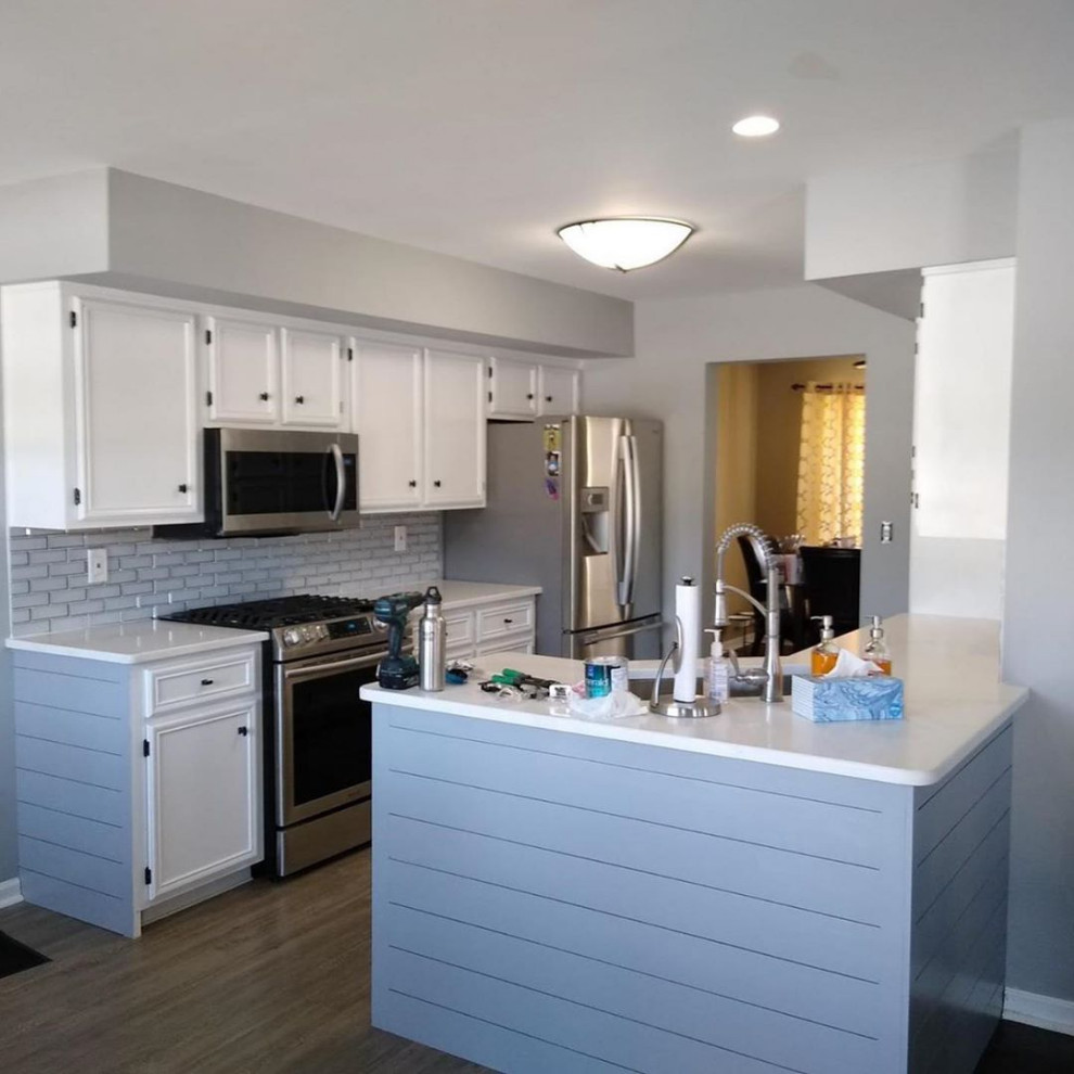 Example of a mid-sized minimalist laminate floor, brown floor and vaulted ceiling kitchen design in Philadelphia with white cabinets, granite countertops, white backsplash, subway tile backsplash, stainless steel appliances and white countertops