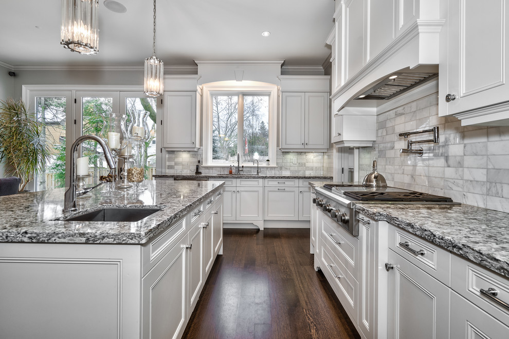 Example of a large transitional u-shaped dark wood floor and brown floor open concept kitchen design in Toronto with an undermount sink, beaded inset cabinets, white cabinets, granite countertops, gray backsplash, marble backsplash, paneled appliances, an island and multicolored countertops
