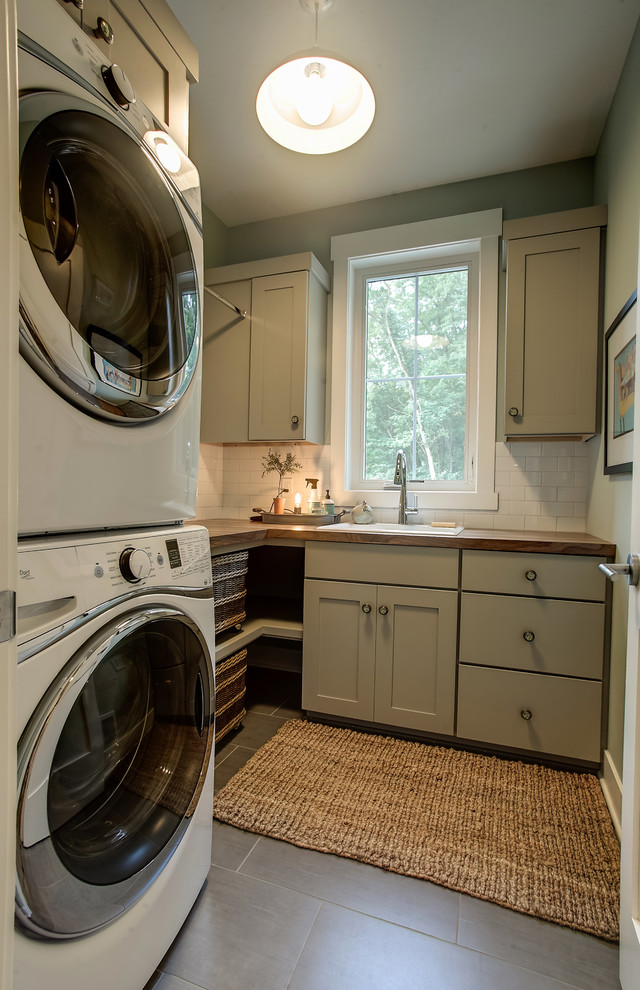 Photo of a small midcentury l-shaped dedicated laundry room in Grand Rapids with a drop-in sink, shaker cabinets, beige cabinets, wood benchtops, grey walls, a stacked washer and dryer and beige floor.