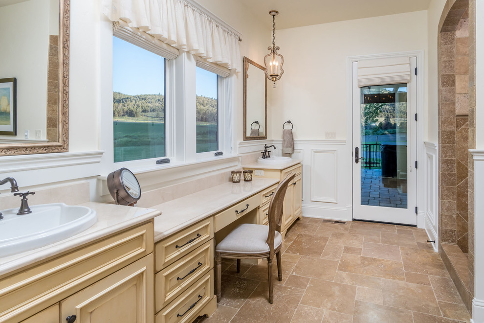 This is an example of a large master bathroom in Other with raised-panel cabinets, beige cabinets, brown tile, limestone, beige walls, limestone floors, a drop-in sink and brown floor.