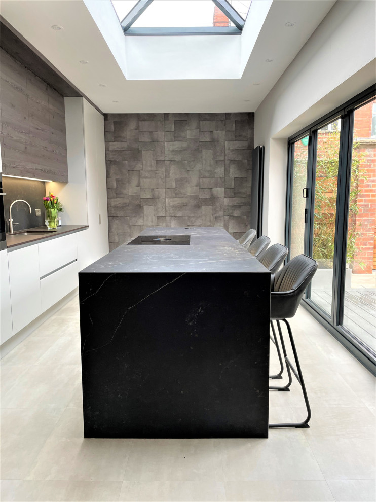 This is an example of a large contemporary grey and brown single-wall open plan kitchen in Other with a single-bowl sink, flat-panel cabinets, medium wood cabinets, engineered stone countertops, grey splashback, black appliances, vinyl flooring, an island, grey floors, grey worktops and a chimney breast.