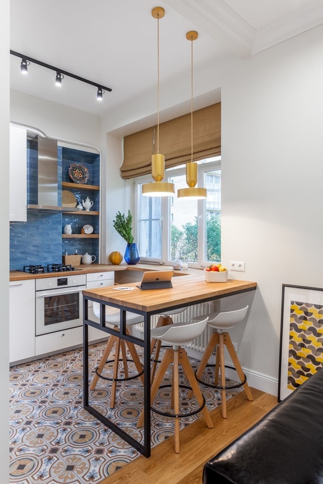Mid-sized contemporary l-shaped eat-in kitchen in Moscow with a single-bowl sink, flat-panel cabinets, white cabinets, wood benchtops, blue splashback, ceramic splashback, white appliances, ceramic floors, no island, multi-coloured floor and brown benchtop.