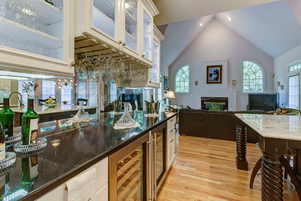Inspiration for a mid-sized transitional galley light wood floor eat-in kitchen remodel in Raleigh with a double-bowl sink, raised-panel cabinets, white cabinets, granite countertops, white backsplash, stone tile backsplash, stainless steel appliances and an island