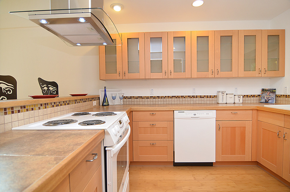 This is an example of a mid-sized arts and crafts u-shaped open plan kitchen in Seattle with a double-bowl sink, shaker cabinets, light wood cabinets, tile benchtops, beige splashback, ceramic splashback, white appliances, bamboo floors and a peninsula.