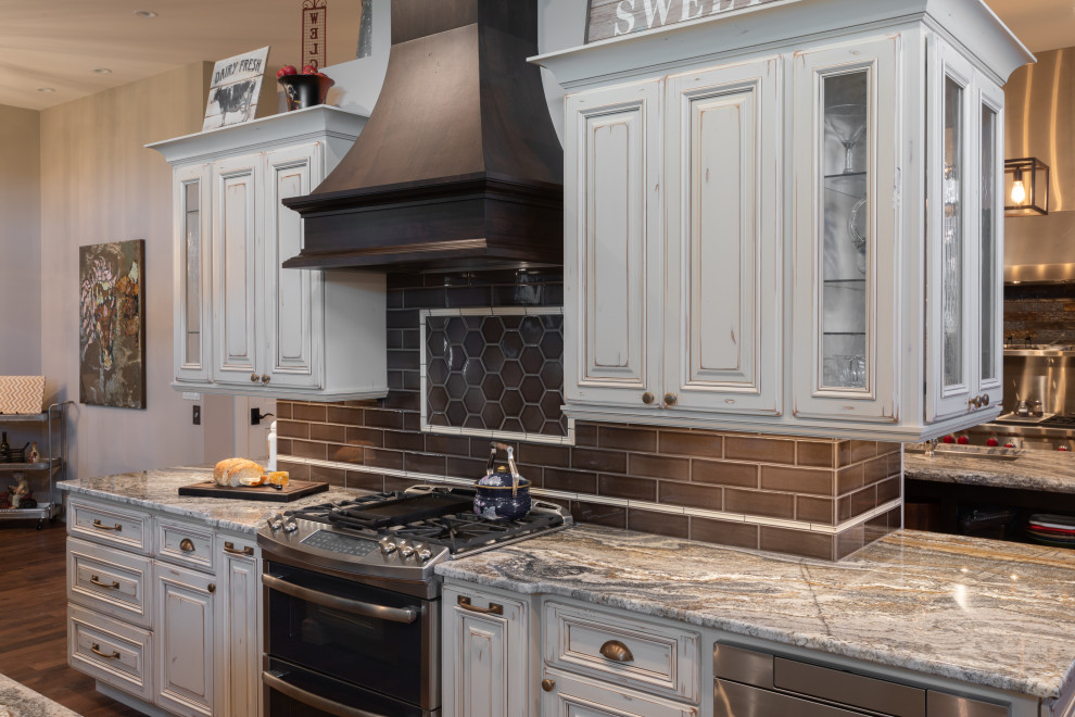 Design ideas for a large country u-shaped kitchen in Omaha with granite benchtops, stainless steel appliances, multiple islands, a double-bowl sink, raised-panel cabinets, distressed cabinets, brown splashback, subway tile splashback, dark hardwood floors, brown floor and grey benchtop.