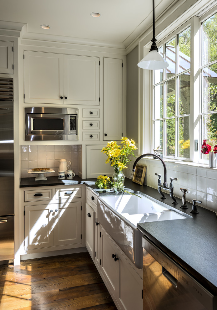 Photo of a traditional eat-in kitchen in New York with a farmhouse sink, shaker cabinets, grey cabinets, soapstone benchtops, white splashback, porcelain splashback and stainless steel appliances.