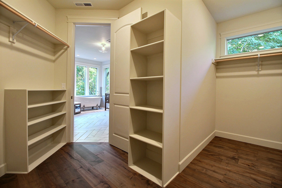 Photo of an expansive arts and crafts gender-neutral walk-in wardrobe in Portland with open cabinets, white cabinets, dark hardwood floors and brown floor.