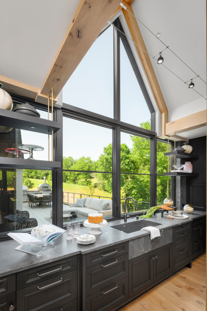 Moderne Küche mit schwarzen Schränken, Quarzit-Arbeitsplatte, Küchengeräten aus Edelstahl, hellem Holzboden, zwei Kücheninseln und freigelegten Dachbalken in Minneapolis
