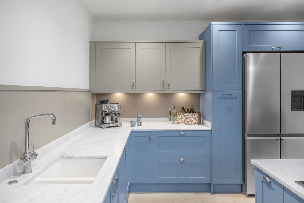 Photo of a large nautical l-shaped kitchen/diner in Other with an integrated sink, shaker cabinets, blue cabinets, composite countertops, beige splashback, black appliances, porcelain flooring, an island, beige floors and white worktops.