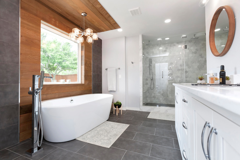 Photo of a mid-sized contemporary master bathroom in Dallas with shaker cabinets, white cabinets, a freestanding tub, a double shower, a one-piece toilet, gray tile, porcelain tile, grey walls, porcelain floors, a drop-in sink, grey floor, a hinged shower door and engineered quartz benchtops.