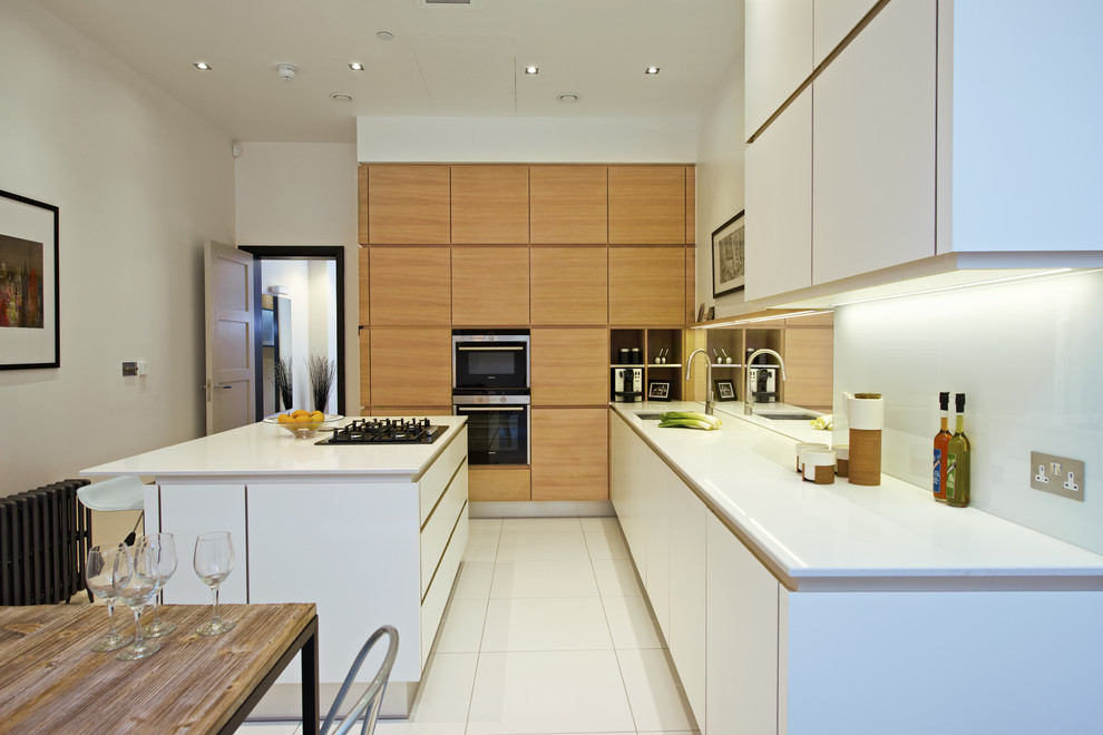 Inspiration for a mid-sized contemporary l-shaped eat-in kitchen in London with flat-panel cabinets, medium wood cabinets, white splashback, glass sheet splashback, stainless steel appliances, ceramic floors, with island, a single-bowl sink, solid surface benchtops, white floor and white benchtop.