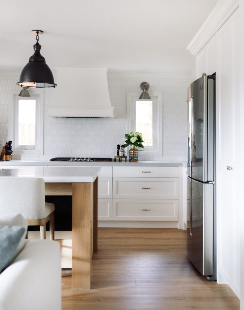 Imagen de cocina tradicional renovada de tamaño medio con fregadero sobremueble, armarios estilo shaker, puertas de armario blancas, encimera de cuarzo compacto, salpicadero blanco, salpicadero de azulejos de cerámica, electrodomésticos de acero inoxidable, suelo vinílico, una isla y encimeras blancas