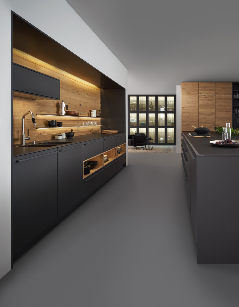 Photo of a large modern single-wall open plan kitchen in Vancouver with an integrated sink, flat-panel cabinets, black cabinets, timber splashback, black appliances, concrete floors and with island.