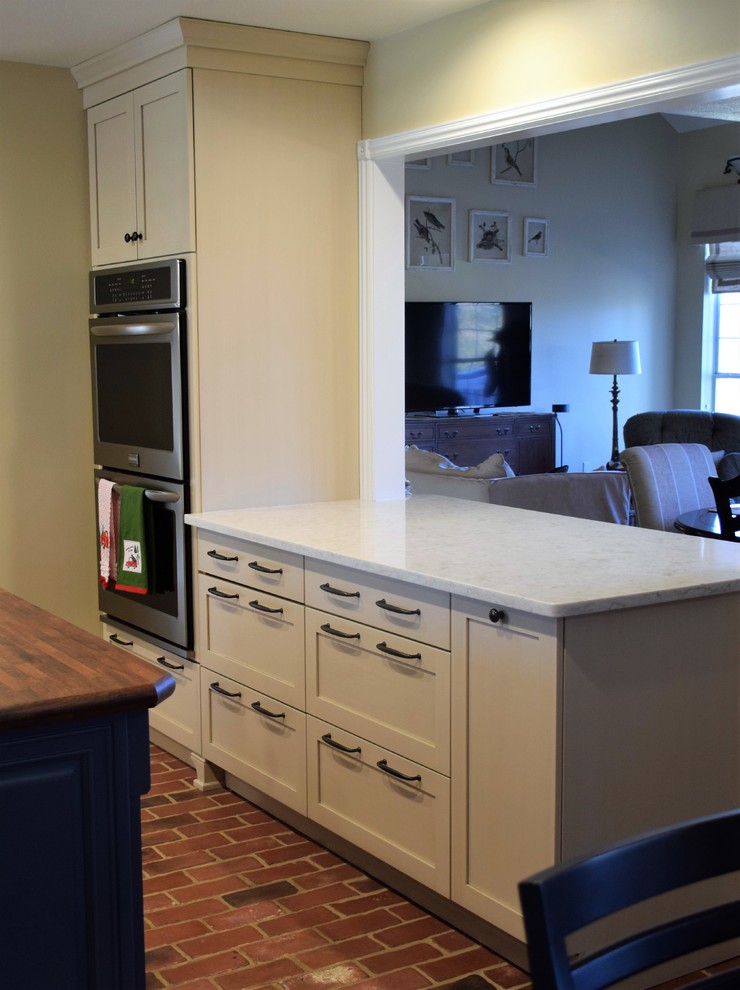 Inspiration for a mid-sized transitional u-shaped brick floor eat-in kitchen remodel with a farmhouse sink, shaker cabinets, white cabinets, quartzite countertops, white backsplash, subway tile backsplash, stainless steel appliances and an island