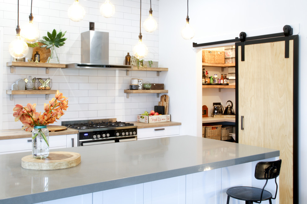 Mid-sized eclectic galley kitchen pantry in Other with a farmhouse sink, shaker cabinets, white cabinets, laminate benchtops, white splashback, subway tile splashback, stainless steel appliances, laminate floors, with island and brown floor.