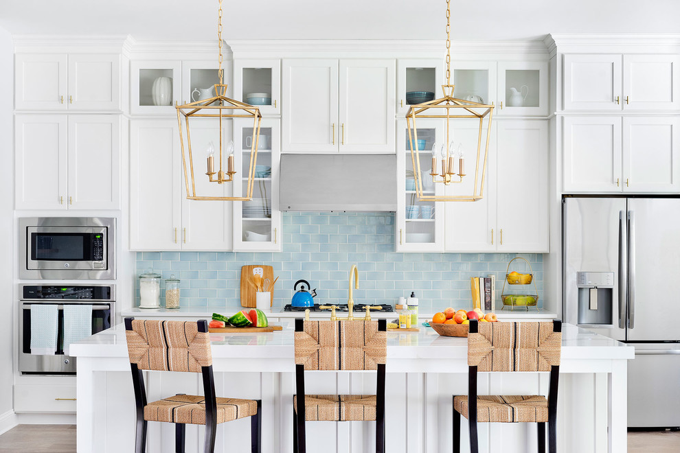 This is an example of a large transitional galley open plan kitchen in Jacksonville with a double-bowl sink, beaded inset cabinets, white cabinets, soapstone benchtops, blue splashback, subway tile splashback, stainless steel appliances, light hardwood floors, with island and brown floor.