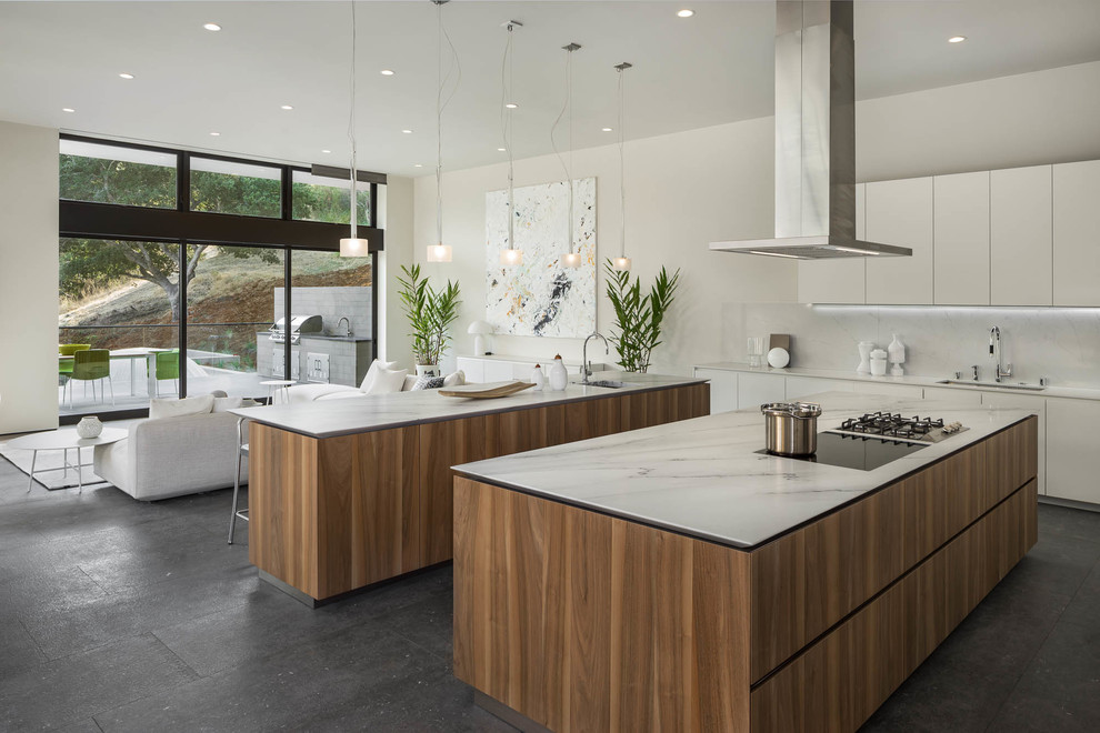 This is an example of a contemporary l-shaped open plan kitchen in San Francisco with an undermount sink, flat-panel cabinets, white cabinets, white splashback, multiple islands, grey floor and white benchtop.