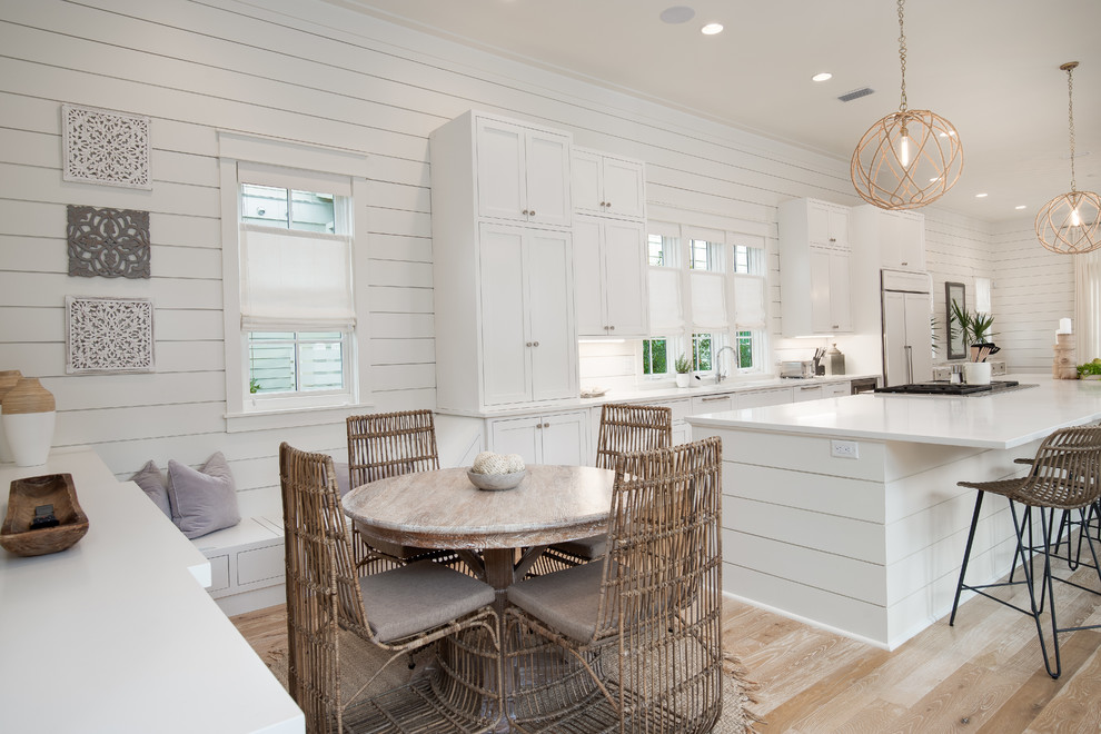 Inspiration for a beach style eat-in kitchen with shaker cabinets, white cabinets, panelled appliances, light hardwood floors, with island, beige floor and white benchtop.