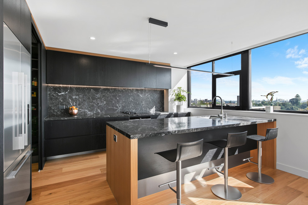 This is an example of a contemporary l-shaped kitchen in Melbourne with an undermount sink, flat-panel cabinets, black cabinets, black splashback, stainless steel appliances, medium hardwood floors, a peninsula, brown floor and black benchtop.
