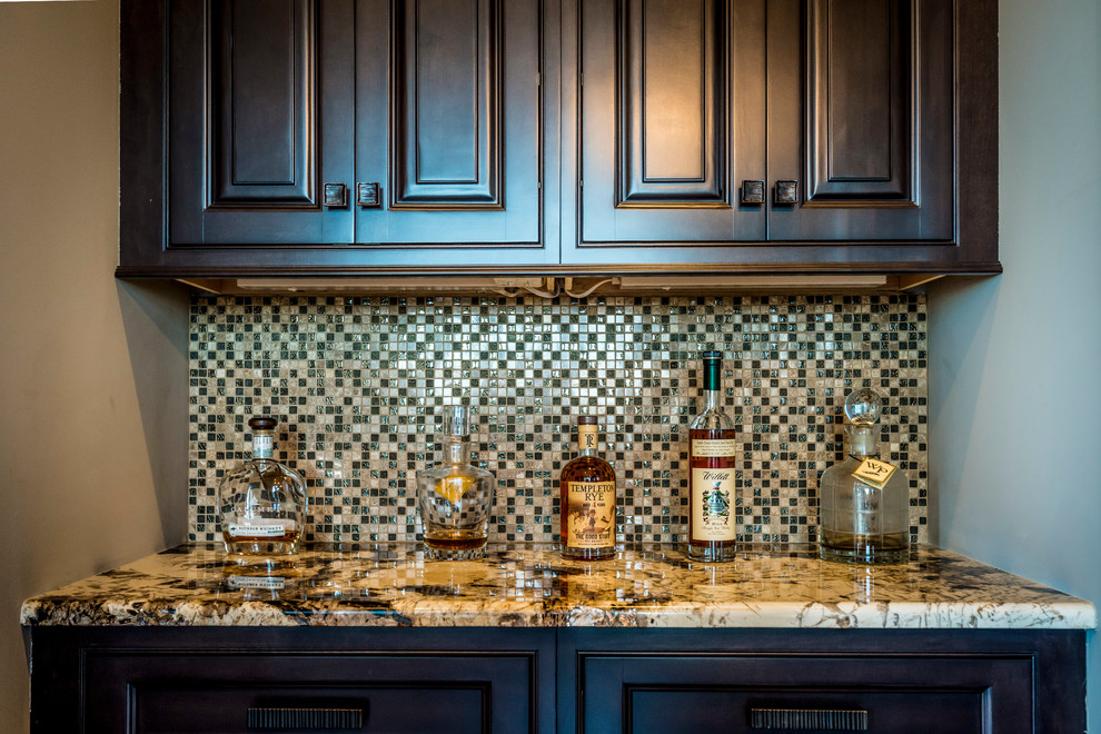 This is an example of a mid-sized galley wet bar in Charleston with an undermount sink, raised-panel cabinets, dark wood cabinets, granite benchtops, brown splashback, mosaic tile splashback, medium hardwood floors and brown floor.