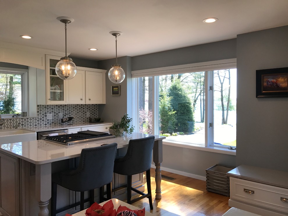 Eat-in kitchen - mid-sized transitional l-shaped medium tone wood floor and brown floor eat-in kitchen idea with a farmhouse sink, recessed-panel cabinets, white cabinets, marble countertops, gray backsplash, mosaic tile backsplash, stainless steel appliances and an island