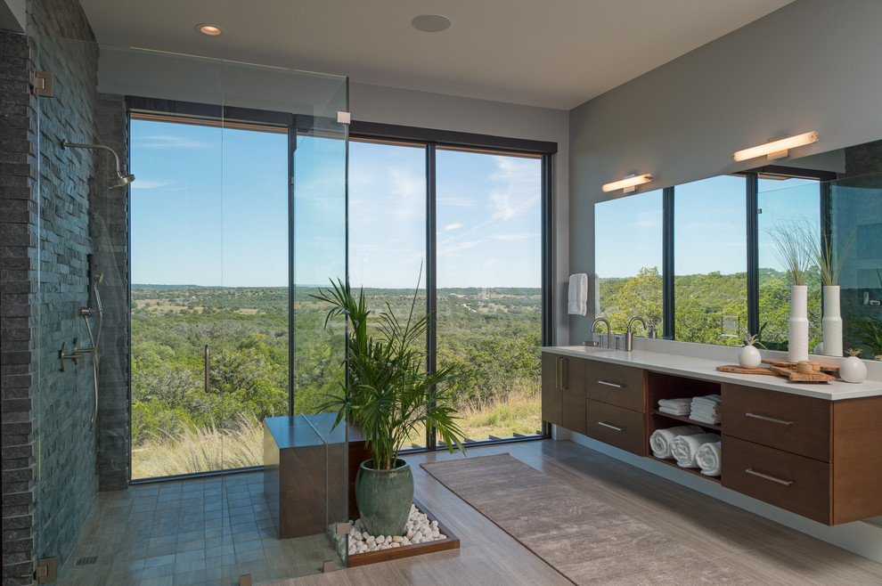 Large contemporary master bathroom in Austin with flat-panel cabinets, medium wood cabinets, a curbless shower, grey walls, a hinged shower door, white benchtops, gray tile, stone tile, an integrated sink, engineered quartz benchtops, beige floor, a two-piece toilet, medium hardwood floors and a shower seat.