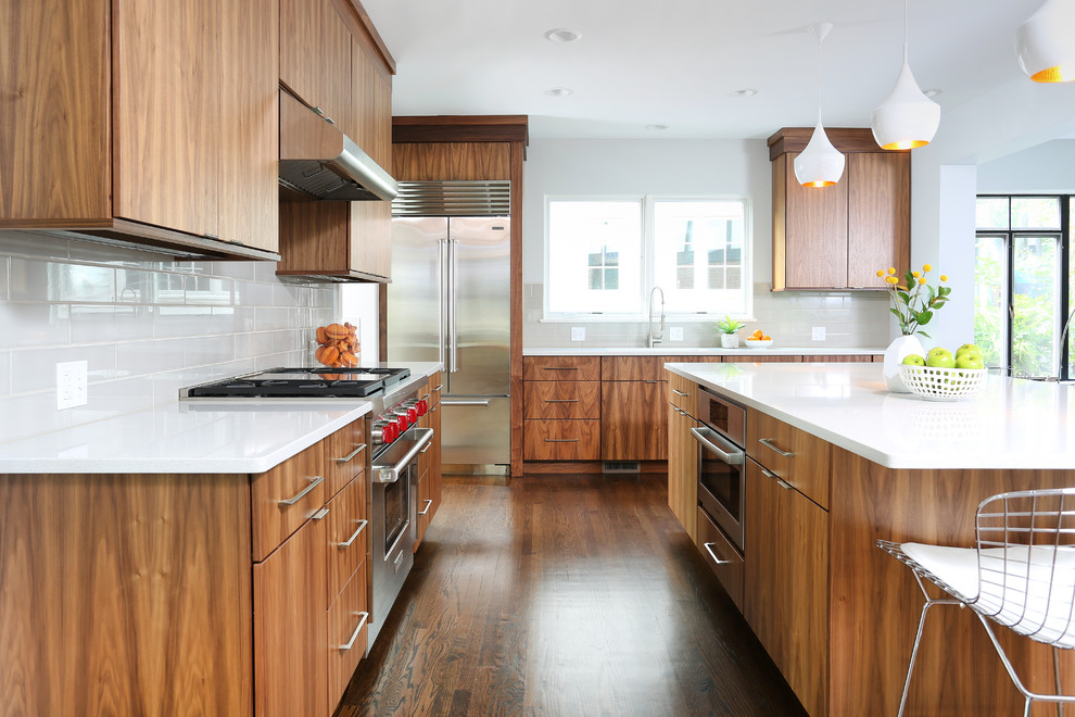 Large midcentury l-shaped eat-in kitchen in Chicago with a single-bowl sink, flat-panel cabinets, brown cabinets, stainless steel appliances, medium hardwood floors, with island, quartz benchtops, white splashback and ceramic splashback.