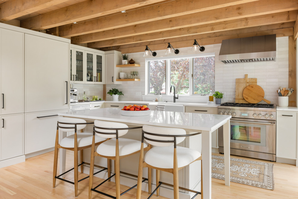 Design ideas for a transitional l-shaped kitchen in Boston with a farmhouse sink, shaker cabinets, grey cabinets, quartz benchtops, white splashback, ceramic splashback, panelled appliances, light hardwood floors, with island, white benchtop, exposed beam and beige floor.