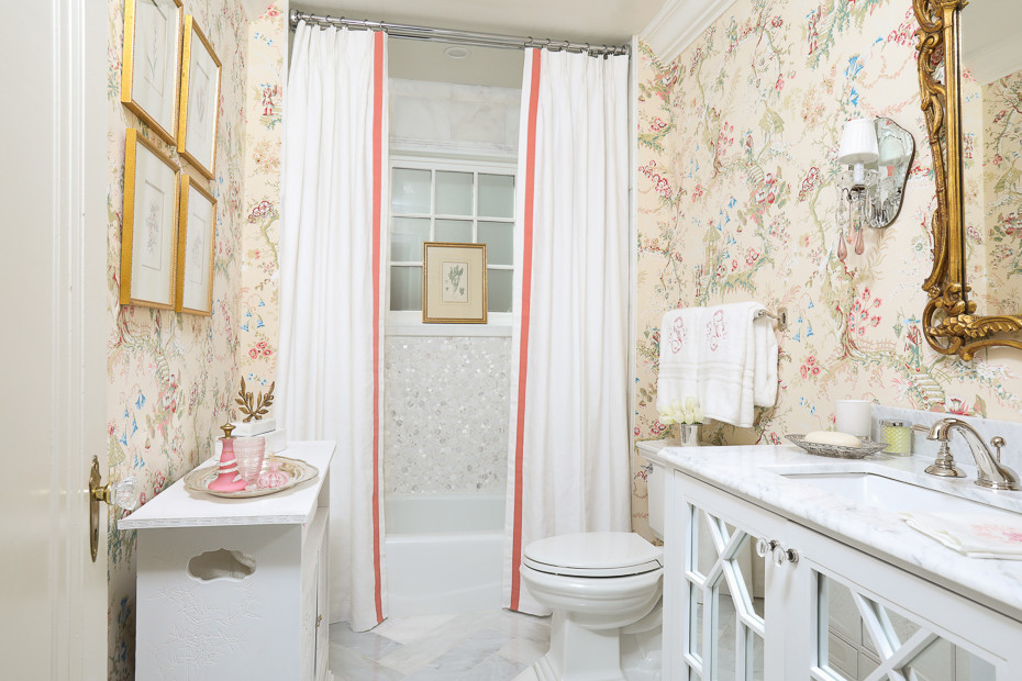 This is an example of a small traditional powder room in Atlanta with glass-front cabinets, white cabinets, a two-piece toilet, white tile, pink walls, marble floors, an undermount sink and marble benchtops.