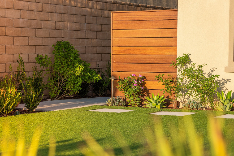 Photo of a mid-sized contemporary front yard full sun xeriscape for spring in Orange County with with lawn edging, concrete pavers and a wood fence.