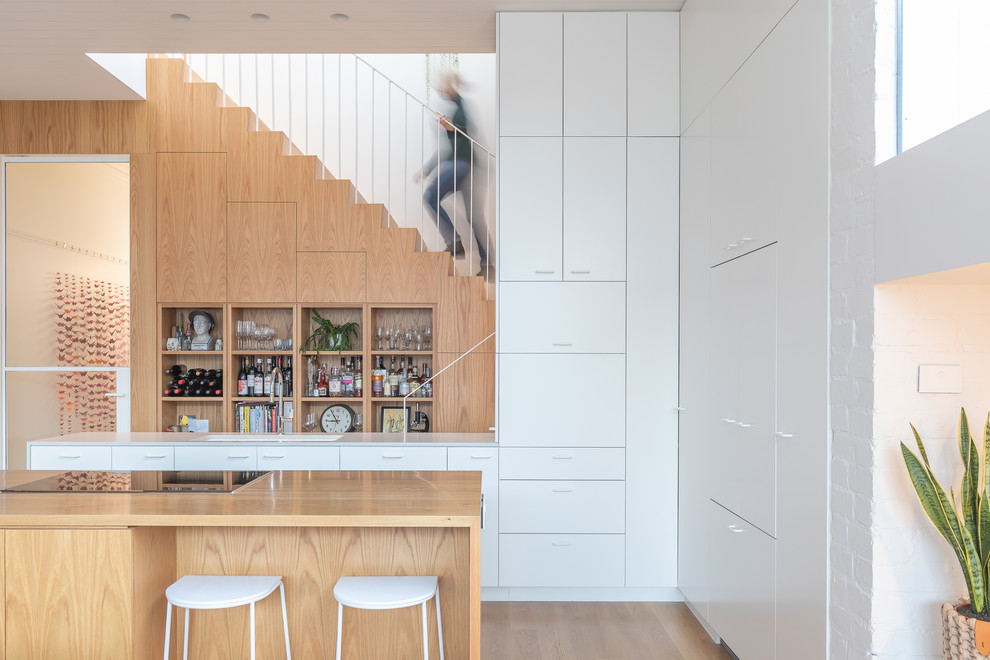 Small contemporary galley kitchen in Melbourne with an undermount sink, recessed-panel cabinets, white cabinets, black appliances, light hardwood floors, multiple islands, brown floor and multi-coloured benchtop.