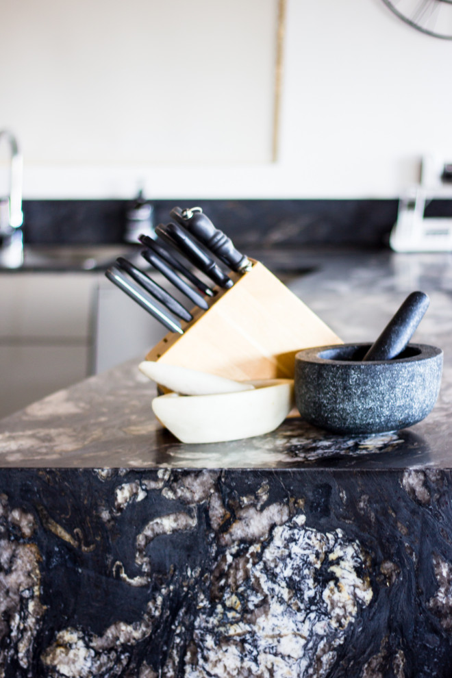 Large modern u-shaped kitchen pantry in Central Coast with a double-bowl sink, flat-panel cabinets, beige cabinets, granite benchtops, metallic splashback, glass sheet splashback, stainless steel appliances, slate floors, a peninsula, brown floor and black benchtop.