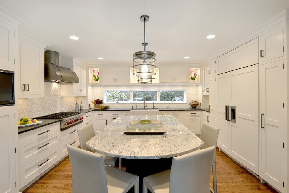 Large industrial u-shaped kitchen in New York with a farmhouse sink, shaker cabinets, white cabinets, granite benchtops, white splashback, porcelain splashback, panelled appliances, medium hardwood floors, with island and brown floor.