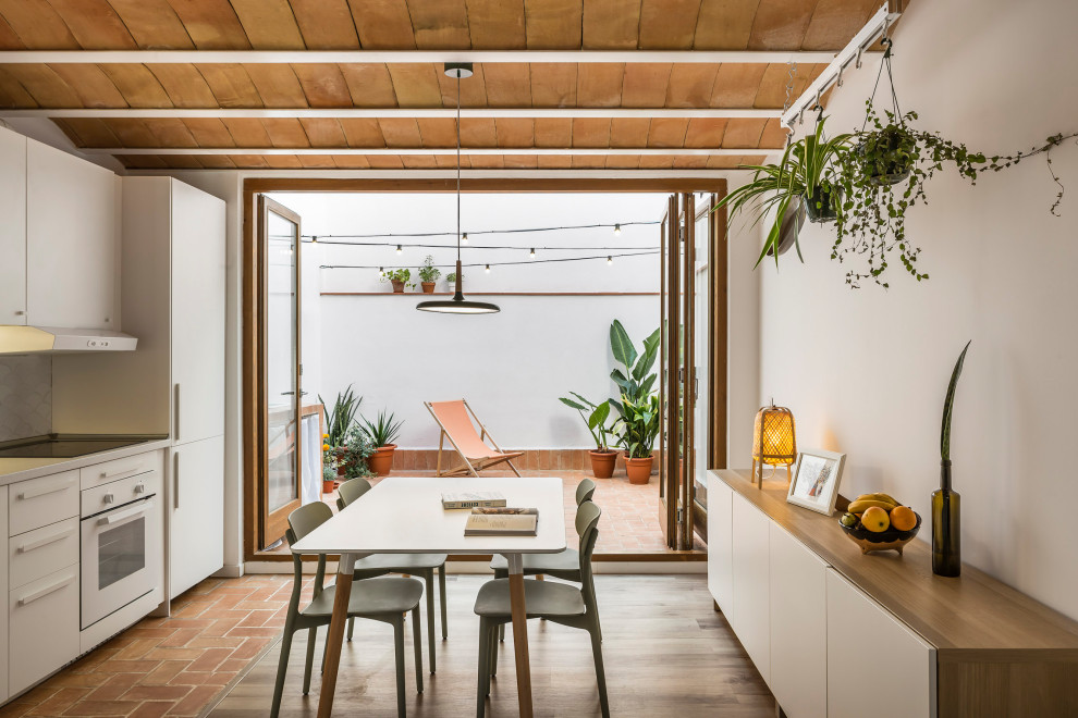 Inspiration for a small mediterranean single-wall open plan kitchen in Valencia with flat-panel cabinets, white cabinets, white splashback, ceramic splashback, white appliances, terracotta flooring, no island, brown floors, white worktops and exposed beams.