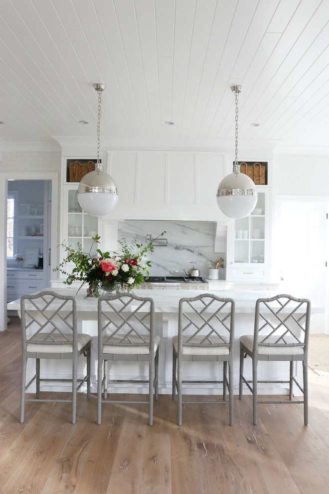 Inspiration for a large country u-shaped eat-in kitchen in Vancouver with white cabinets, stainless steel appliances, with island, a farmhouse sink, recessed-panel cabinets, marble benchtops, white splashback, stone slab splashback, medium hardwood floors and brown floor.