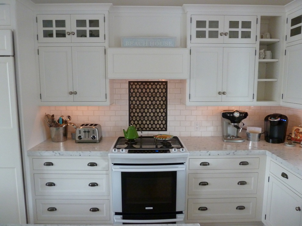 This is an example of a large beach style l-shaped eat-in kitchen in Philadelphia with a farmhouse sink, recessed-panel cabinets, white cabinets, marble benchtops, white splashback, subway tile splashback, white appliances, medium hardwood floors and with island.
