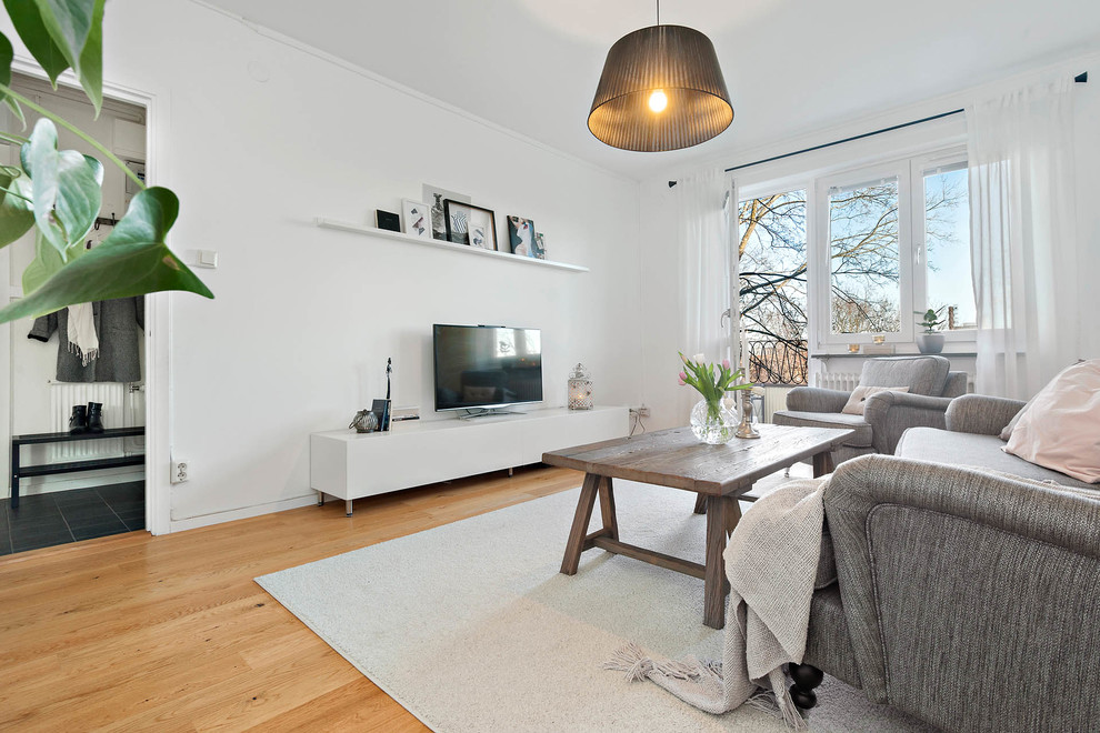 Mid-sized transitional enclosed living room in Stockholm with white walls, medium hardwood floors, a freestanding tv and beige floor.