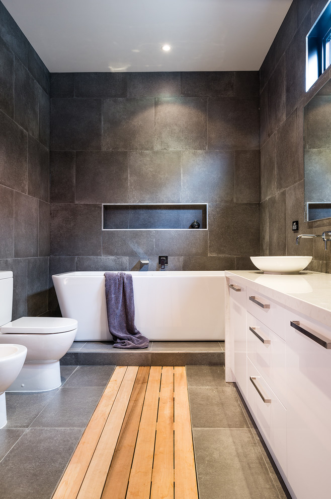 Large contemporary master bathroom in Melbourne with flat-panel cabinets, white cabinets, a freestanding tub, a double shower, a bidet, gray tile, porcelain tile, grey walls, light hardwood floors, a vessel sink, engineered quartz benchtops, grey floor, an open shower and white benchtops.