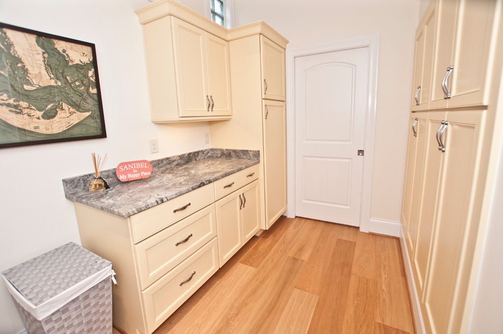 This is an example of a large beach style galley dedicated laundry room in Nashville with flat-panel cabinets, marble benchtops, beige walls, light hardwood floors, a concealed washer and dryer, brown floor, multi-coloured benchtop and beige cabinets.