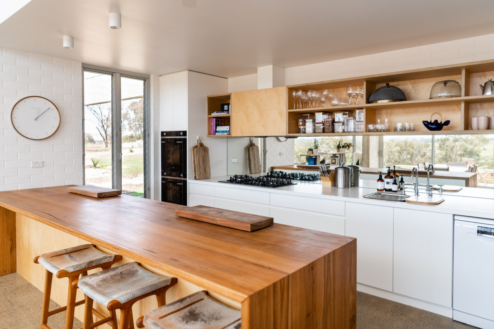 Design ideas for a mid-sized contemporary galley open plan kitchen in Other with a double-bowl sink, white cabinets, wood benchtops, metallic splashback, mirror splashback, white appliances, concrete floors, with island, grey floor, brown benchtop and flat-panel cabinets.