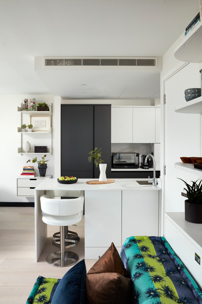 Small contemporary u-shaped open plan kitchen in London with a drop-in sink, flat-panel cabinets, white cabinets, tile benchtops, white splashback, ceramic splashback, stainless steel appliances, light hardwood floors, with island and white benchtop.