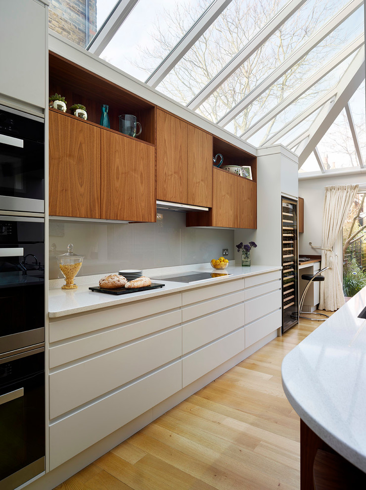 Design ideas for an expansive contemporary open plan kitchen in London with flat-panel cabinets, grey splashback, glass sheet splashback, stainless steel appliances and an island.
