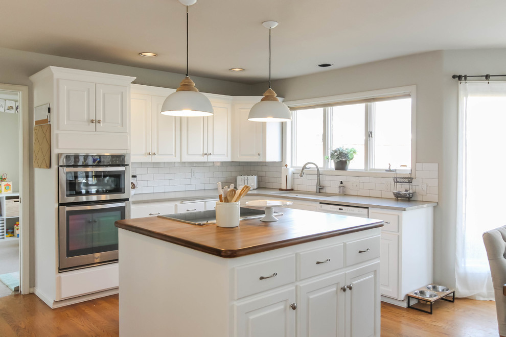 Mid-sized traditional eat-in kitchen in Seattle with an undermount sink, raised-panel cabinets, white cabinets, quartz benchtops, white splashback, subway tile splashback, stainless steel appliances, medium hardwood floors, with island, brown floor and grey benchtop.