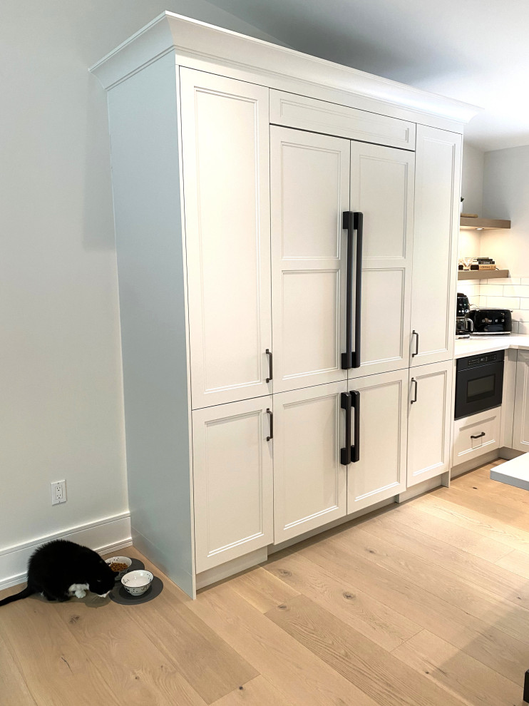 Open concept kitchen - large transitional l-shaped light wood floor and vaulted ceiling open concept kitchen idea in Toronto with an undermount sink, recessed-panel cabinets, white cabinets, quartz countertops, white backsplash, porcelain backsplash, stainless steel appliances, an island and white countertops
